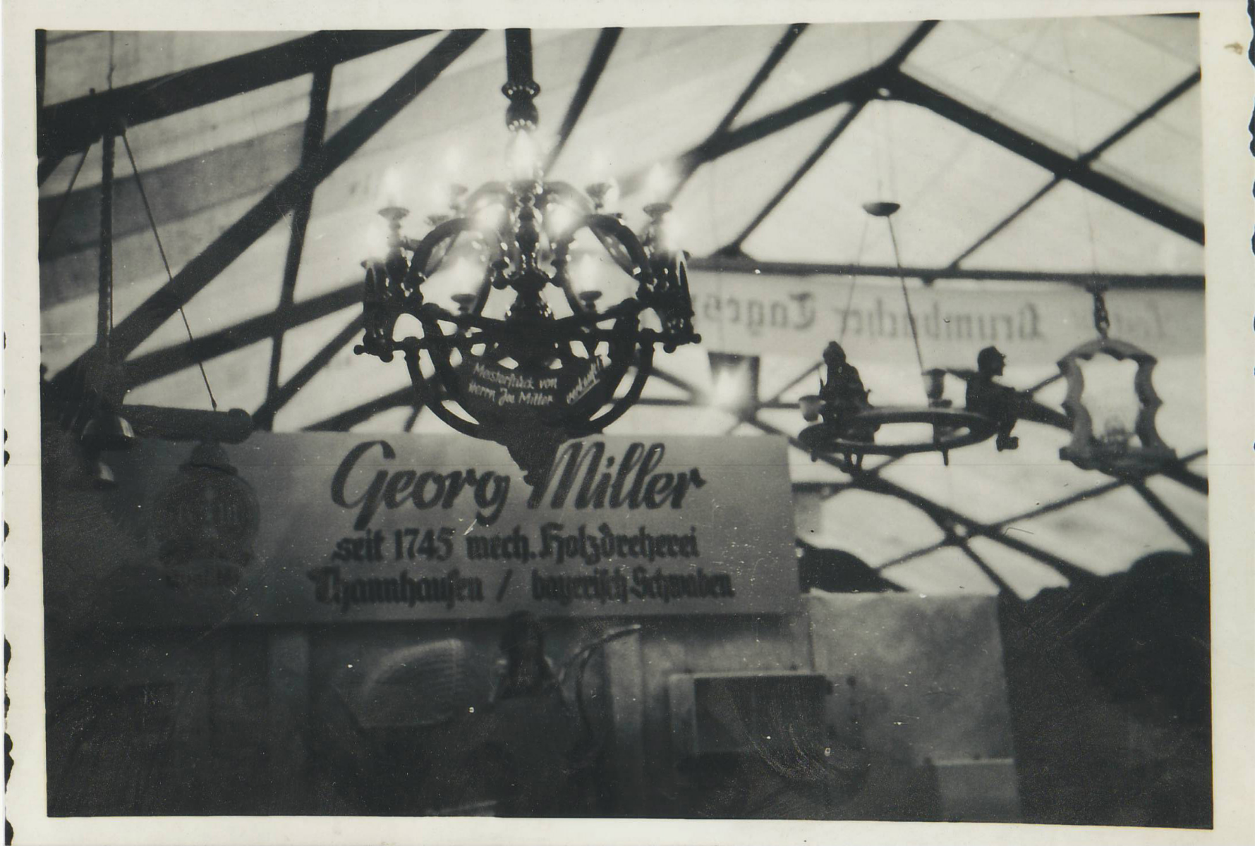 Schwarzweißfoto einer historischen Gewerbeschau der 1950er-Jahre mit einem großen, kunstvoll gedrechselten Kronleuchter und einem Firmenschild der Drechslerei.